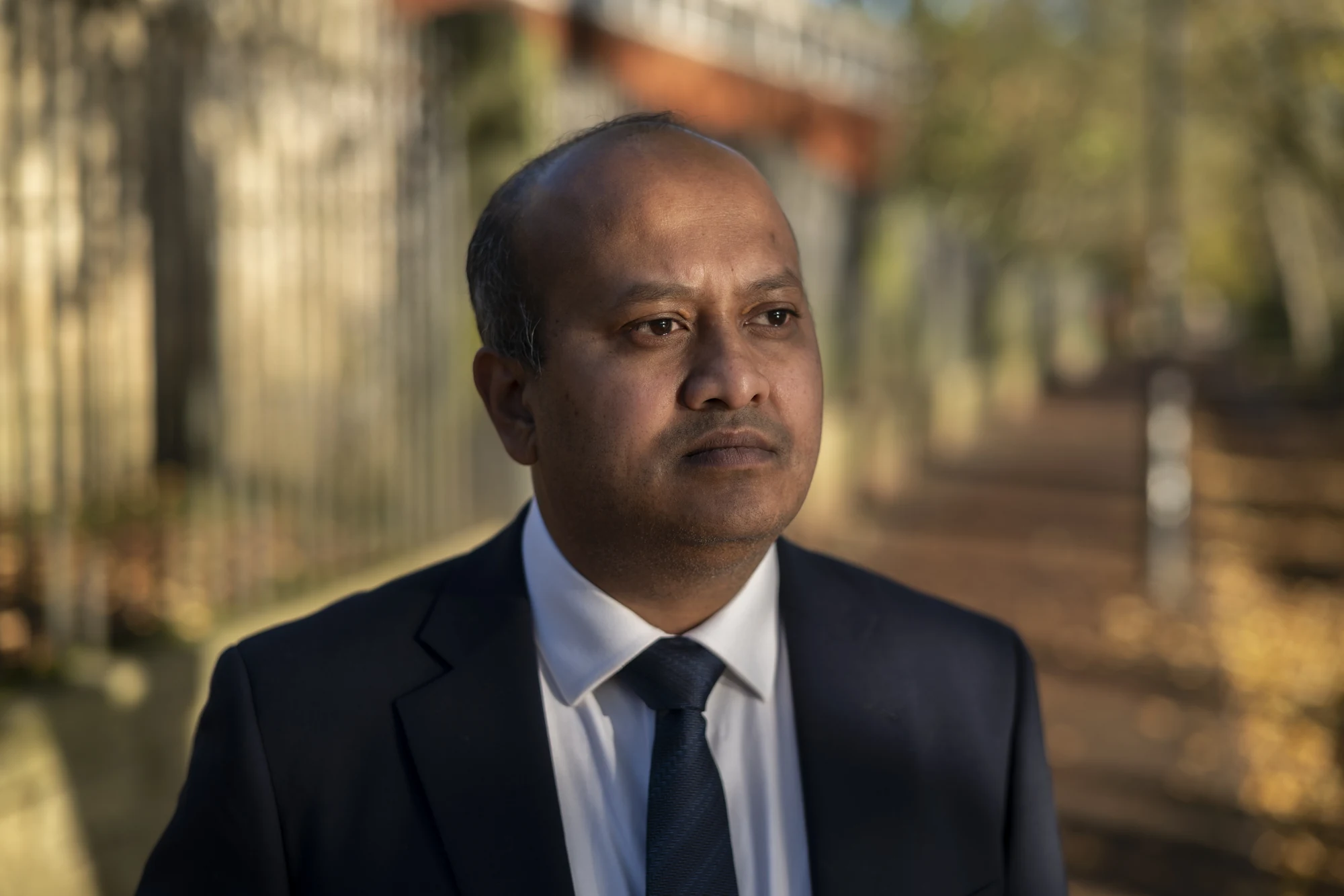 William Gomes in a navy suit beside autumn trees and stone walls